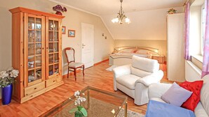 A living room with a wooden cabinet, a white sofa, a chair, and a bed with a headboard. - Ferienwohnung Wesenberg (Wesenberg OT Strasen)