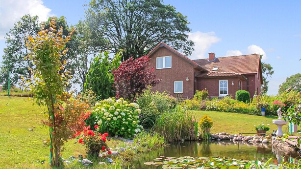 A house with a garden, a pond with lily pads, and a variety of plants. - Ferienwohnung Wesenberg (Wesenberg OT Strasen)