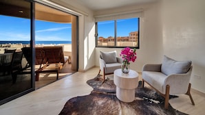 A modern living room with a large glass door leading to a balcony, a round wooden coffee table, two grey armchairs, and a leather rug.