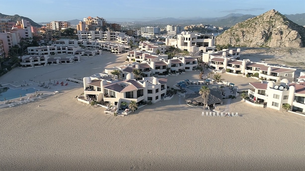 A resort with multiple buildings, a central pool, and a beach area.