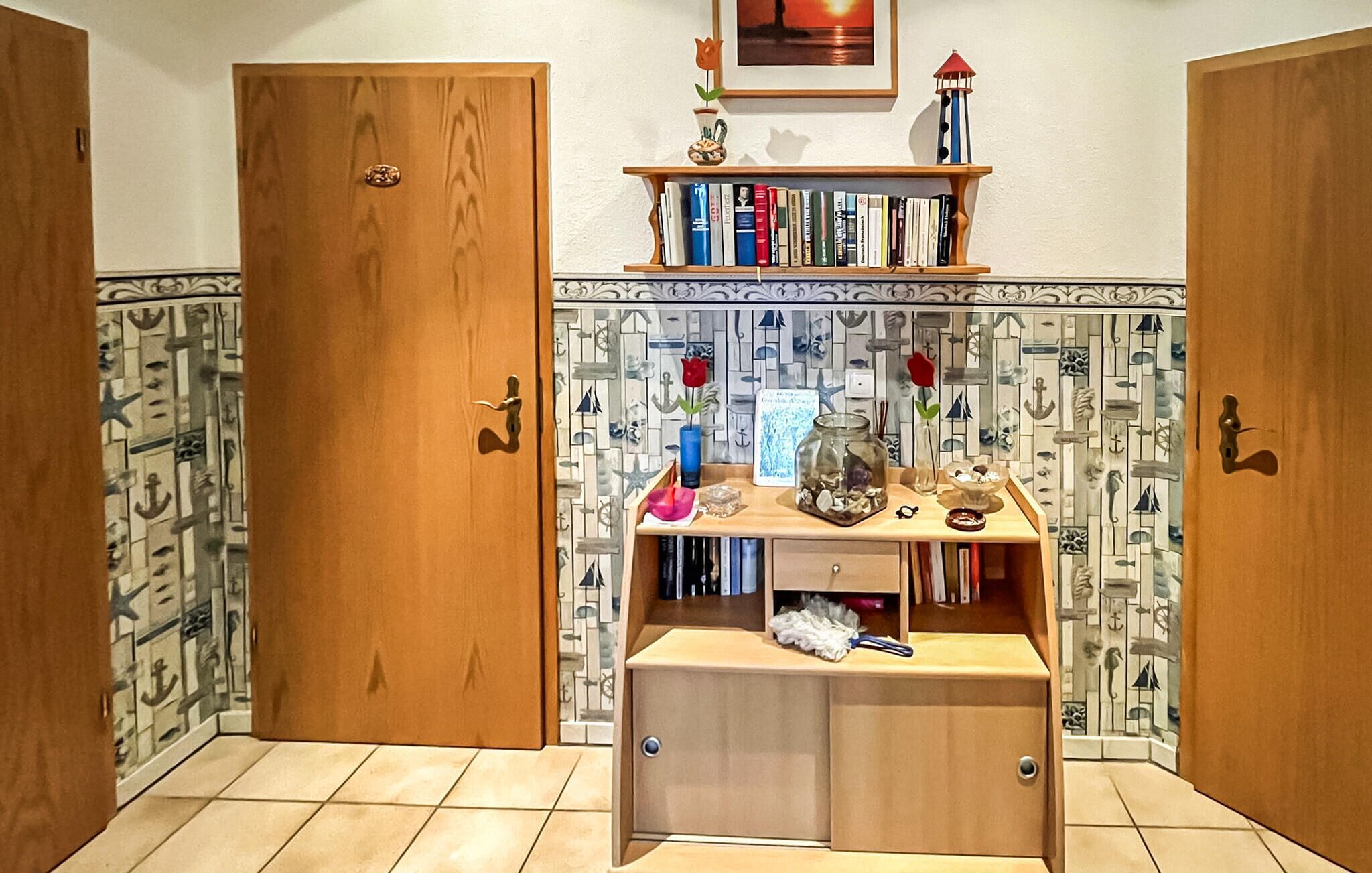 Ein Zimmer mit Holztüren, einem kleinen Schreibtisch mit einer Vase, Büchern und einem gerahmten Bild an der Wand.