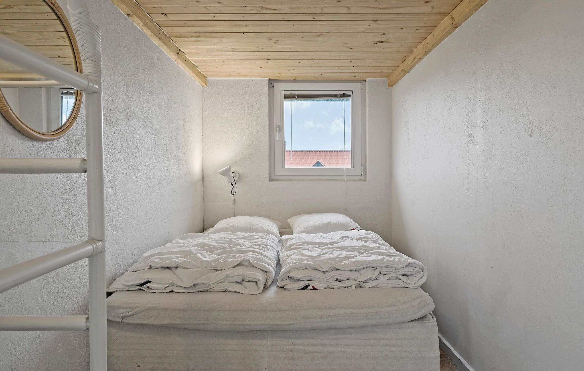 A small, narrow room with a bed, a window, and a mirror.