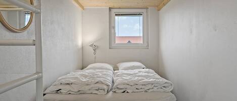 A small, narrow room with a bed, a window, and a mirror.