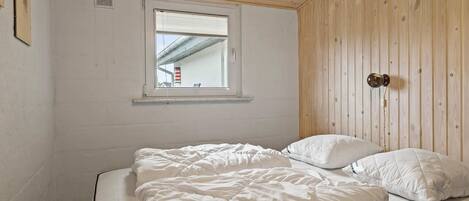 A bedroom with a single bed, a window, wooden walls, and a ceiling with wooden beams.
