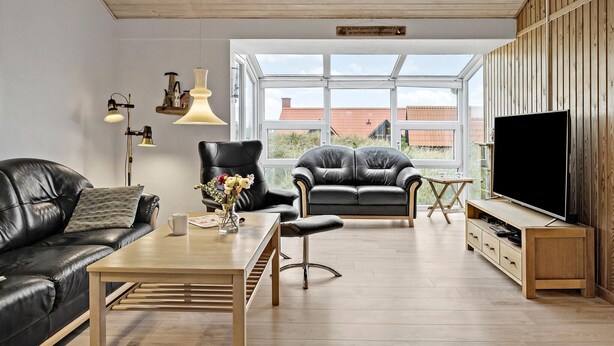 A modern living room with a black leather sofa, a wooden coffee table, a black leather armchair, and a TV stand.