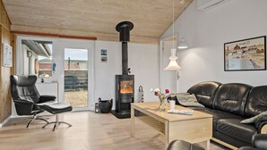 A modern living room with a black wood-burning stove, leather furniture, and a wooden ceiling.