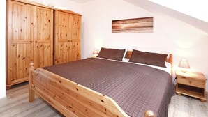 A wooden bed with a quilted cover, two nightstands with lamps, and a wooden wardrobe.