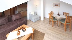 A living area with a sofa, a dining table with chairs, a small kitchenette, and a lamp.