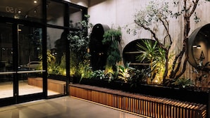 A modern indoor space with a glass entrance, a wooden bench, and various indoor plants. - Cascada (Portland)
