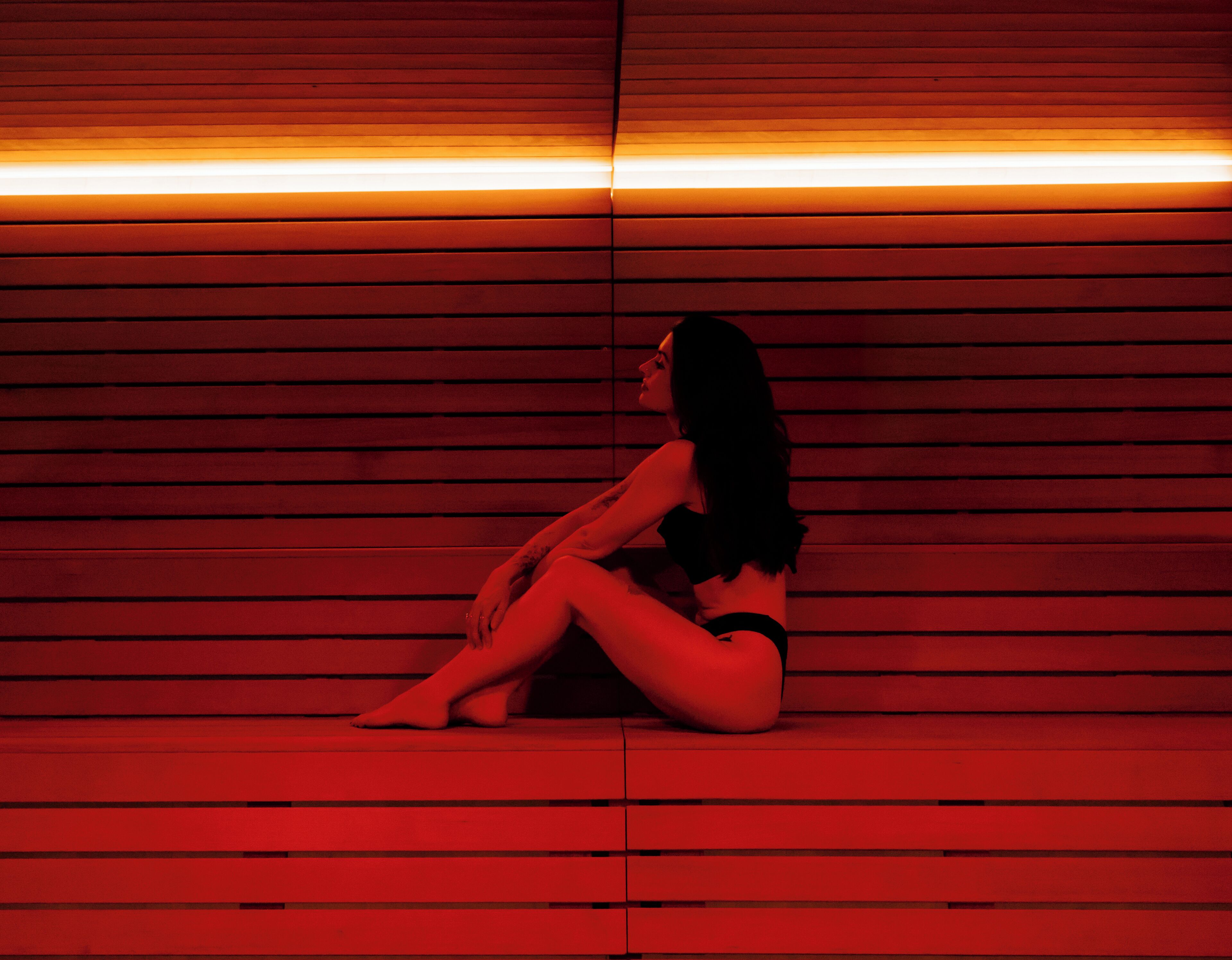 Una persona seduta su una panca in una stanza con rivestimenti in legno e una luce rossa.