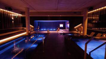 A modern indoor pool area with multiple pools, a central stage, and ambient lighting.