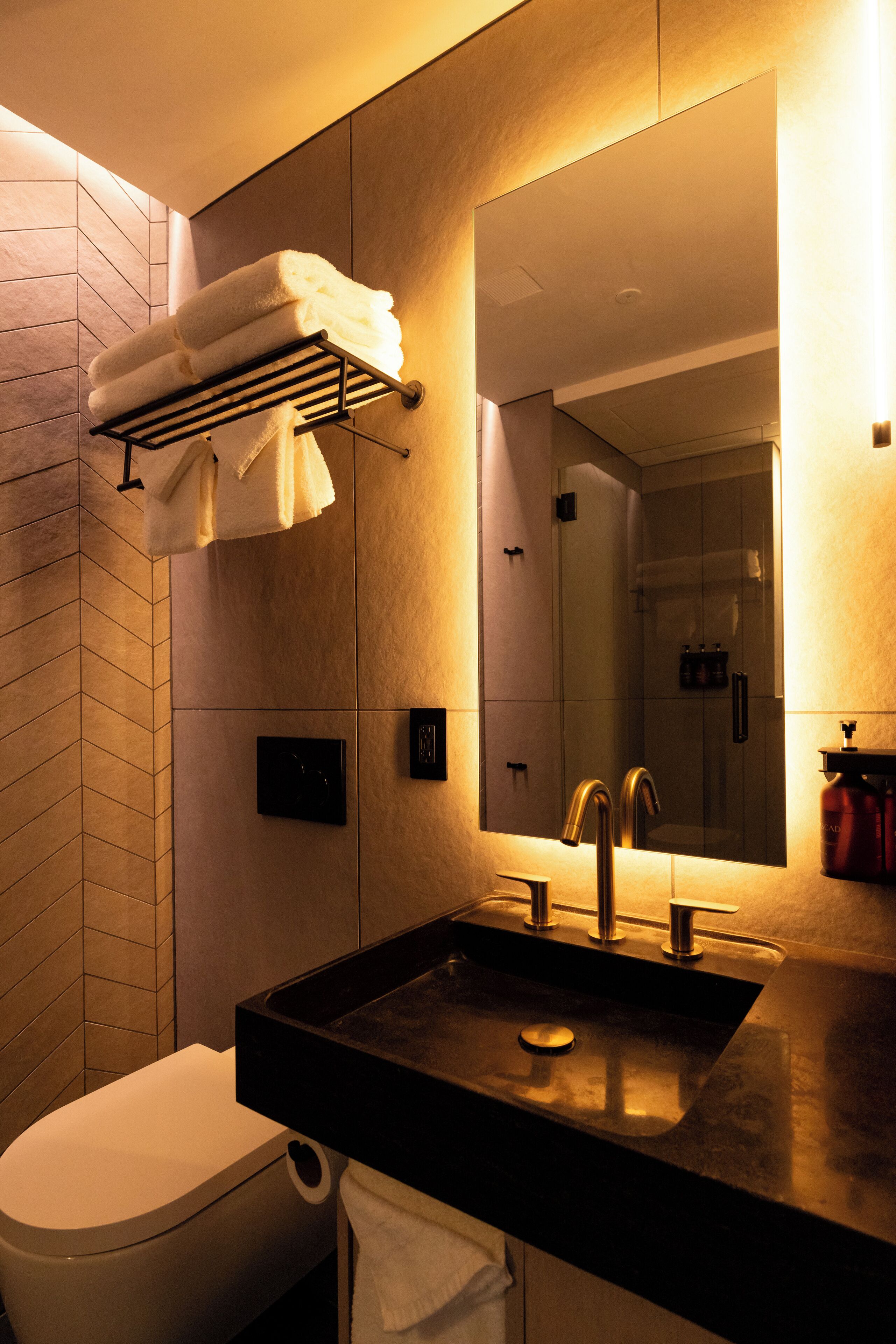 A modern bathroom with a black sink, a toilet, a towel rack with folded towels, a mirror, and a shower area.