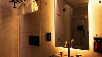 A modern bathroom with a black sink, a toilet, a towel rack with folded towels, a mirror, and a shower area.
