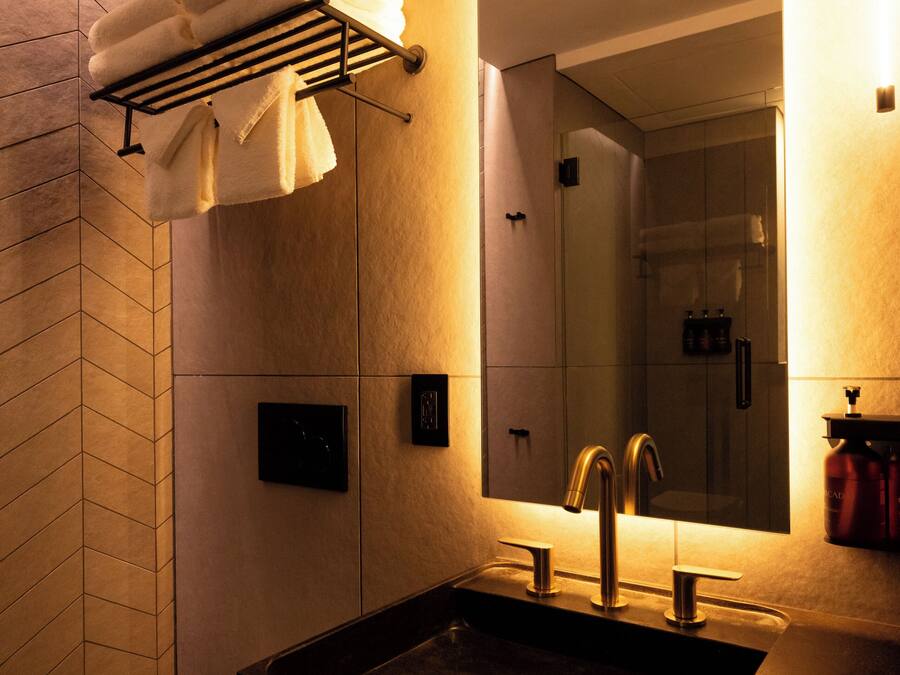 A modern bathroom with a black sink, a toilet, a towel rack with folded towels, a mirror, and a shower area.