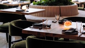 A restaurant interior with tables set for dining, a central plant, and hanging pendant lights. - Cascada (Portland)