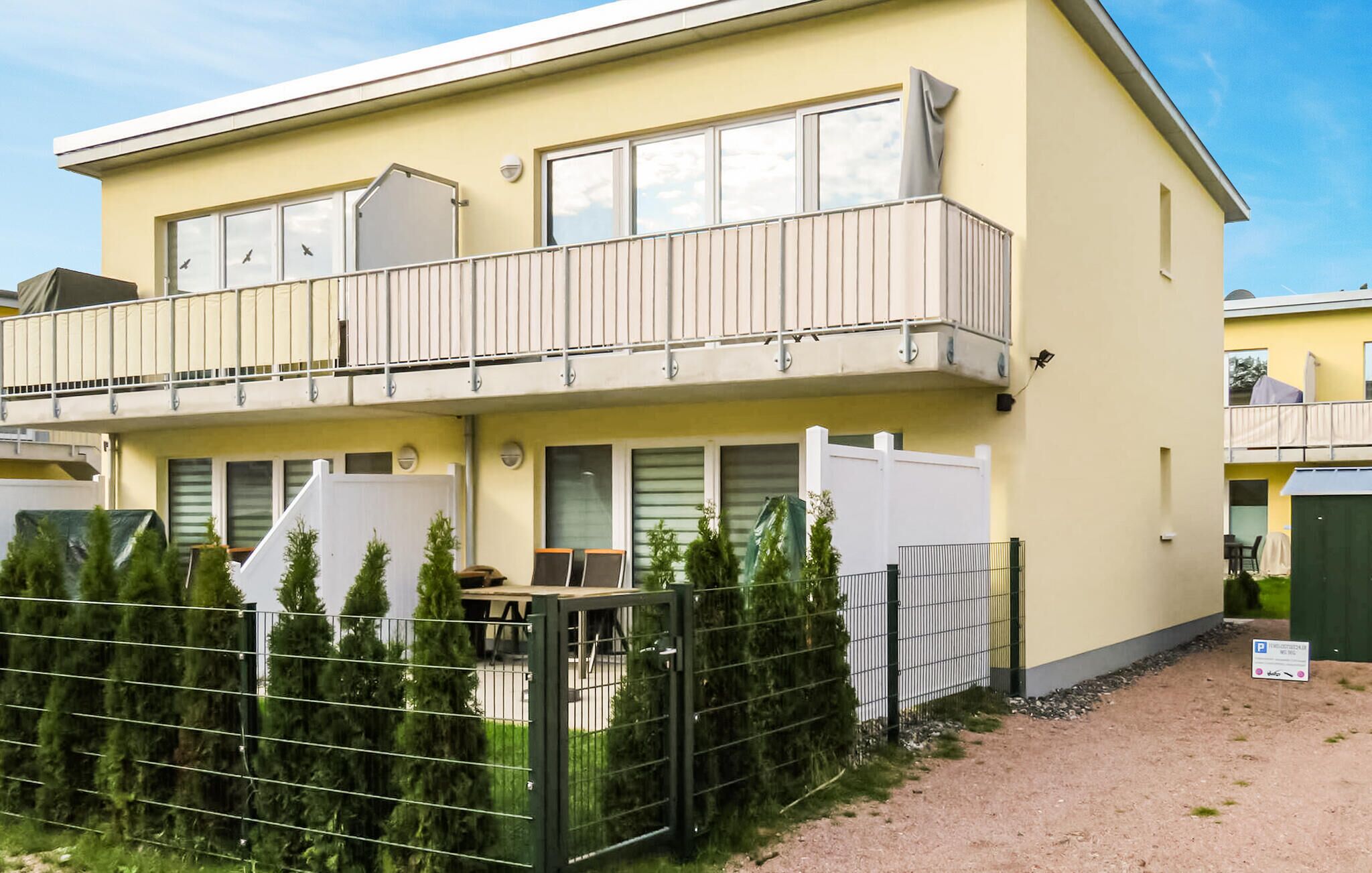 Ein zweistöckiges Gebäude mit Balkon, umzäunter Garten und einem Schild, das freie Parkplätze anzeigt.