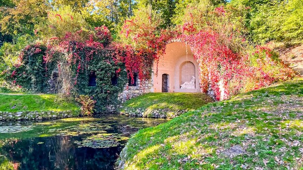 A serene garden with a pond, a stone wall, and a small arched structure covered in flowering vines. - Ferienwohnung Rheinsberg (Rheinsberg)