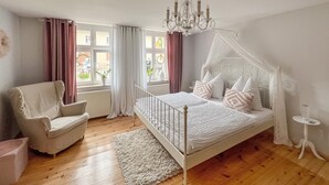 A bedroom with a four-poster bed, a chair, a small table, and a chandelier. - Ferienwohnung Rheinsberg (Rheinsberg)
