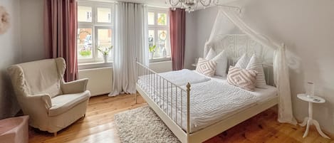 Ein Schlafzimmer mit einem Himmelbett, einem Sessel, einem kleinen Tisch und einer Chandelier.