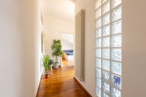 A hallway with wooden flooring, a radiator, a potted plant, and a window with a view of a bed.