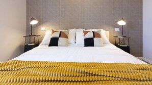 Uma cama bem arrumada com um cobertor estampado, duas luminárias de cabeceira e uma parede com textura.
