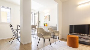 Uma sala de estar moderna com televisão de tela plana, duas poltronas, uma mesa de centro e um banquinho laranja.