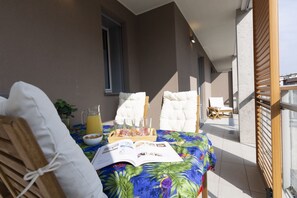 Parvekkeella on aamiaiselle katettu pöytä, jonka päällä on kirja, hedelmäkulho ja mehukannu.