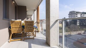 Varanda com cadeiras e mesa de madeira, janelas amplas e vista para um estacionamento.