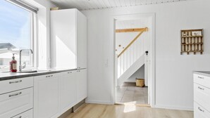 Eine moderne Küche mit weißen Schränken, Holzboden und Blick in den Wohnbereich durch eine offene Tür.