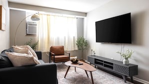 Ein modernes Wohnzimmer mit einem schwarzen Sofa, einem braunen Ledersessel, einem Holztisch und einer schwarzen Unterhaltungsecke, an der eine große Flachbildfernseher angebracht ist.