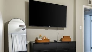Ein Schlafzimmer mit Bett, Schminktisch, Spiegel und einem an der Wand befestigten Flachbildfernseher.
