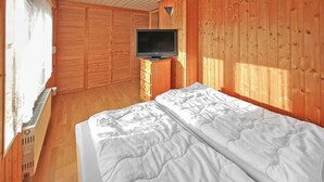 Une pièce en bois avec un lit, un téléviseur posé sur un meuble et une fenêtre avec des rideaux.