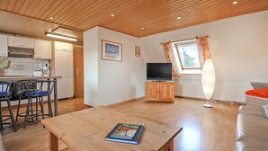 Un salon chaleureux avec un plafond en bois, une télévision, une table à manger avec des chaises et une fenêtre avec des rideaux.
