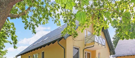 A yellow building with a sloped roof, a staircase leading to the entrance, and a tree with green leaves in the foreground.