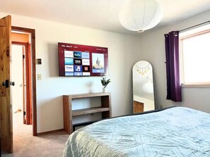 A bedroom with a bed, a TV mounted on the wall, a wooden door, and a window with curtains. - Taos retreat with steam shower and mountain views (El Prado)
