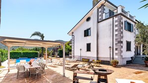 Una casa de dos plantas con piscina, mobiliario de exterior y una pérgola.