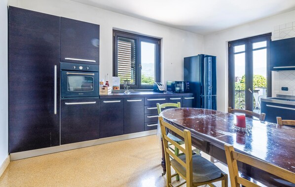 A modern kitchen with dark cabinetry, a built-in oven, a microwave, and a dining area with a table and chairs.