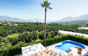 A pool area with lounge chairs and a view of vineyards and mountains.