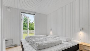 Une chambre à coucher avec un lit, une table de chevet en bois et une fenêtre donnant sur un paysage verdoyant.