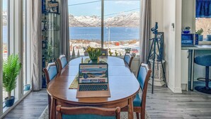 A dining area with a view of mountains and a lake, a laptop on the table, and a telescope on the right.