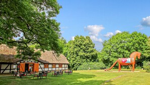 A traditional building with a thatched roof, outdoor seating area, and a wooden horse sculpture. - Ferienwohnung Ankershagen (Ankershagen OT Friedri)