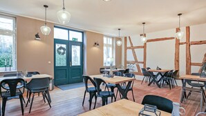 A modern dining area with wooden tables and black chairs, large windows, and a door with a green sign. - Ferienwohnung Ankershagen (Ankershagen OT Friedri)