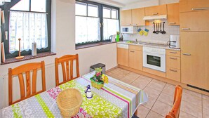 Una cocina con armarios de madera, microondas y horno. Hay una mesa de comedor con sillas y un mantel colorido.