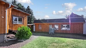 A wooden cabin with a covered porch, a small garden, and a metal roof. - Ferienhaus Trassenheide (Trassenheide (Ostseeba)
