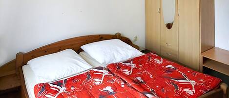Una cama con una colcha de cuadros rojos y blancos, un cabecero de madera y un armario de madera con espejo.