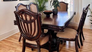 Uma sala de jantar com uma mesa e cadeiras de madeira, obras de arte nas paredes e uma janela com cortinas.