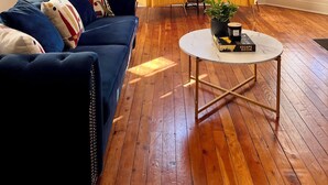 Uma sala de estar com um sofá azul, duas poltronas amarelas, uma mesa de centro branca e um lustre.