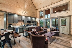 A spacious living area with a wooden ceiling, a kitchen with modern appliances, and large windows offering a view of the outdoors.