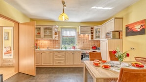 A kitchen with wooden cabinets, a dining table with orange chairs, and a window with plants. - Wohnung Nordwestuckermark (Nordwestuckermark)