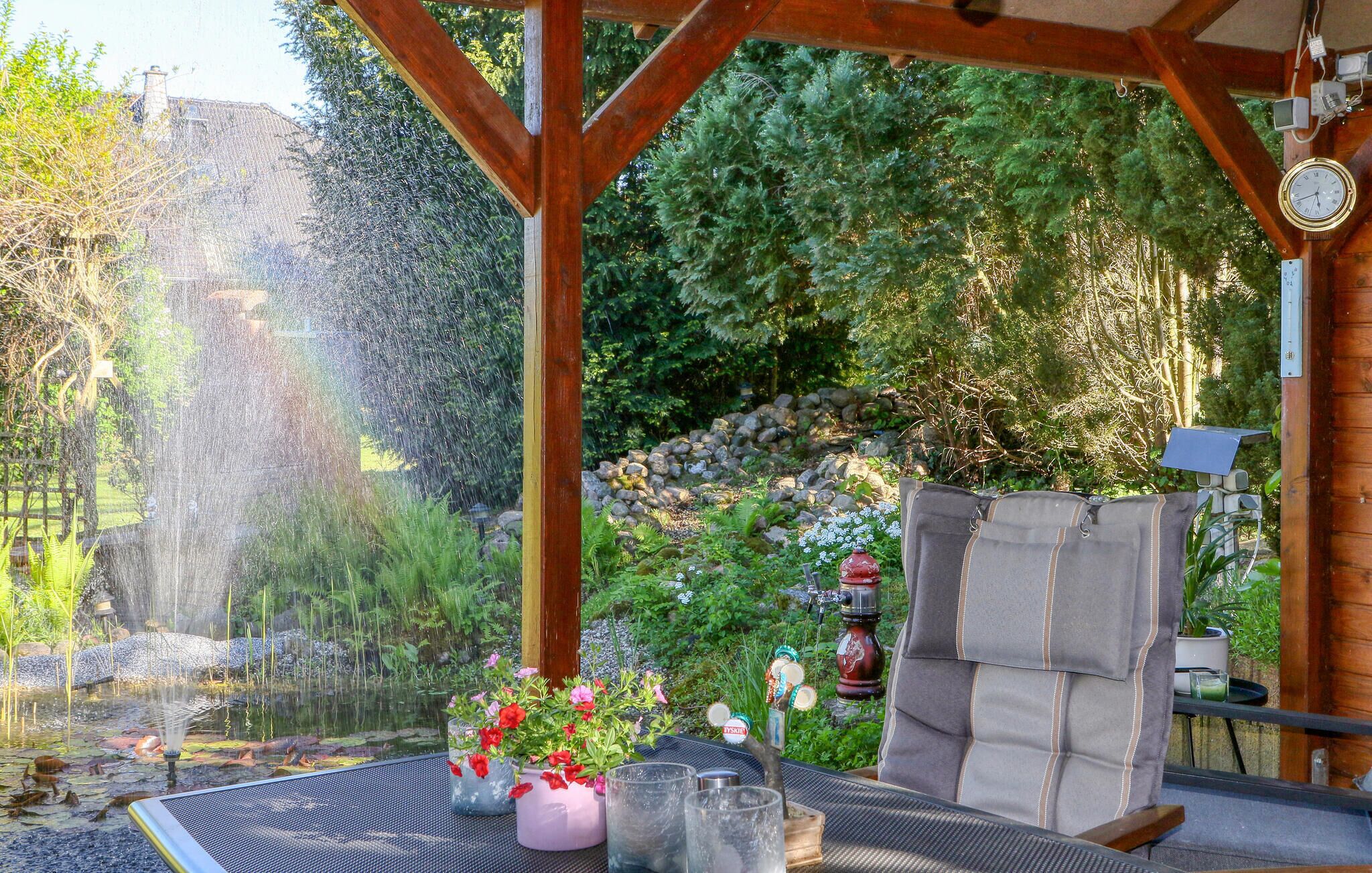 Eine überdachte Terrasse mit Holzkonstruktion, ein kleiner Teich mit Wasserspielen und Kübelpflanzen.
